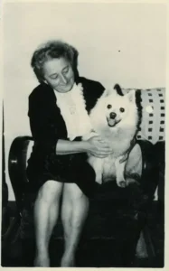 Eine Frau hat ihren Spitz neben sich auf dem Sessel eng umschlungen